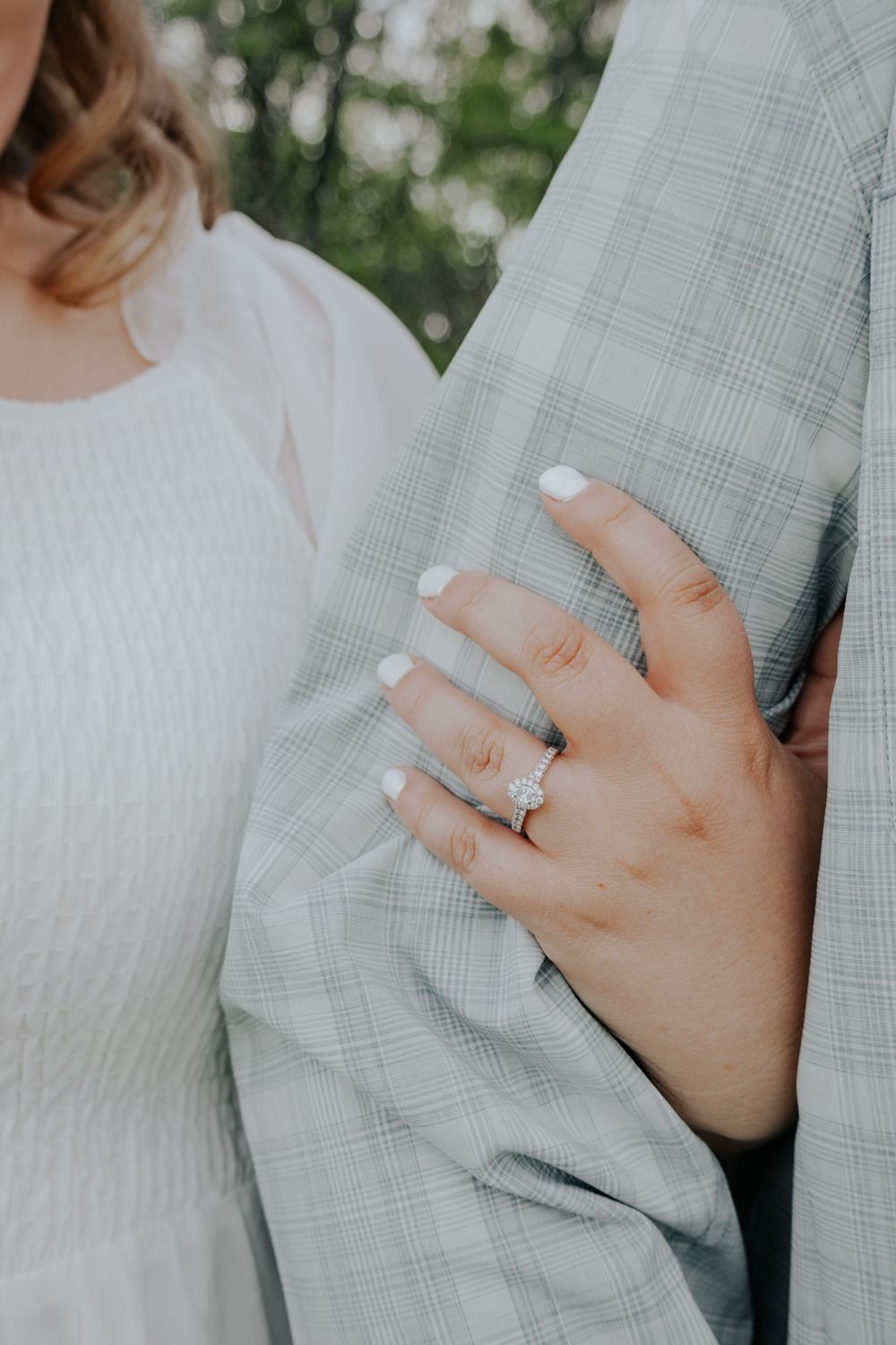 Close-up of a person's hand wearing an engagement ring resting against a grey plaid suit jacket.