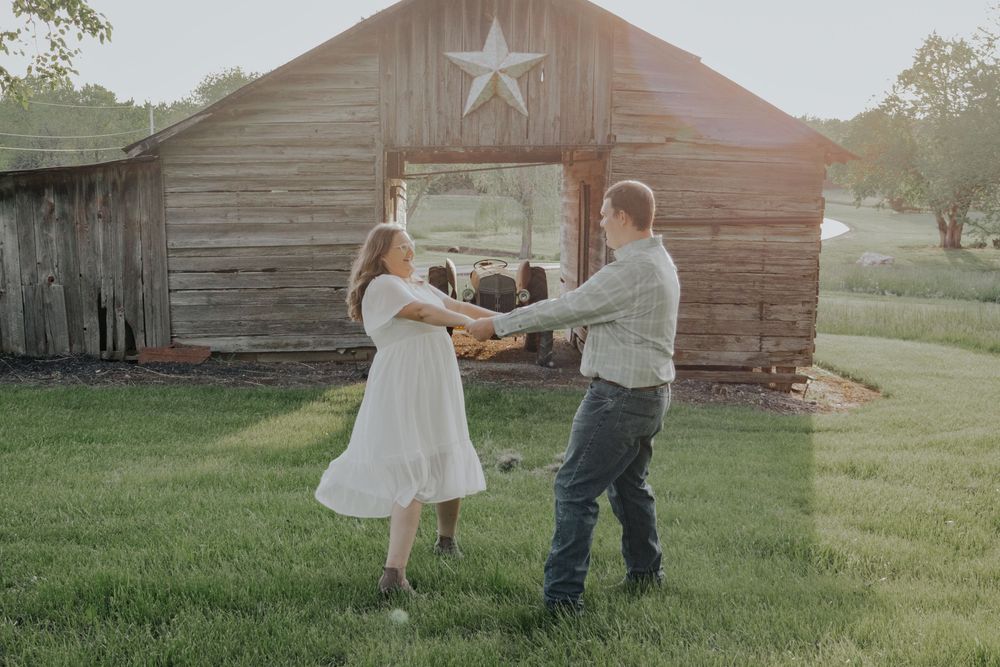 A couple dances together in front of a rustic barn with a star decoration during golden hour.
