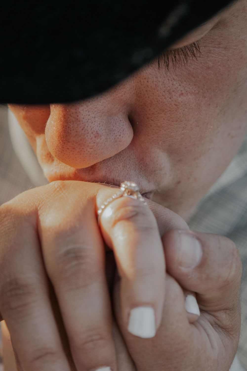 Close-up shot showing hands with white nail polish and engagement ring while covering mouth in emotional moment.
