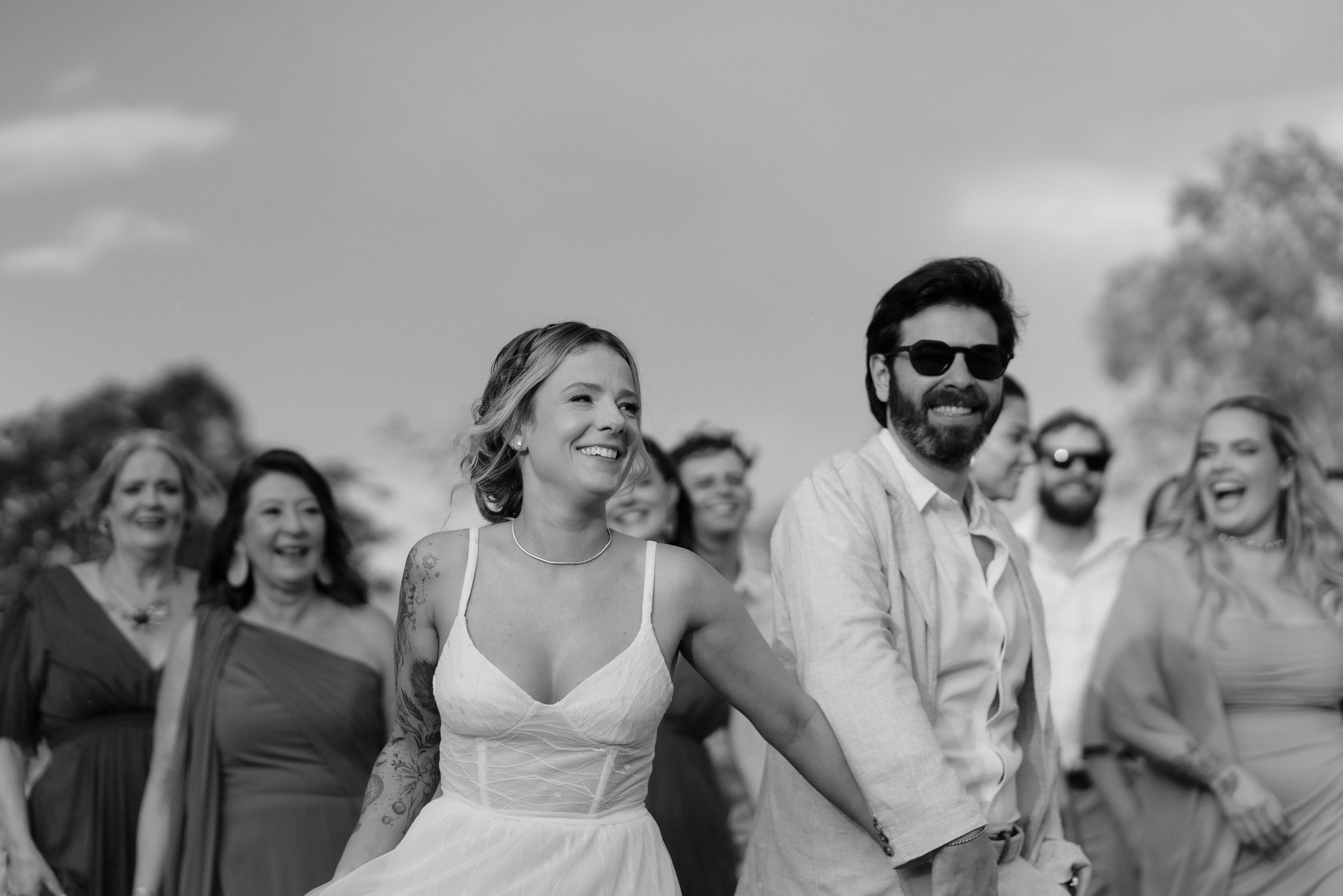 Wedding party walking together outdoors with natural lighting and trees in background.