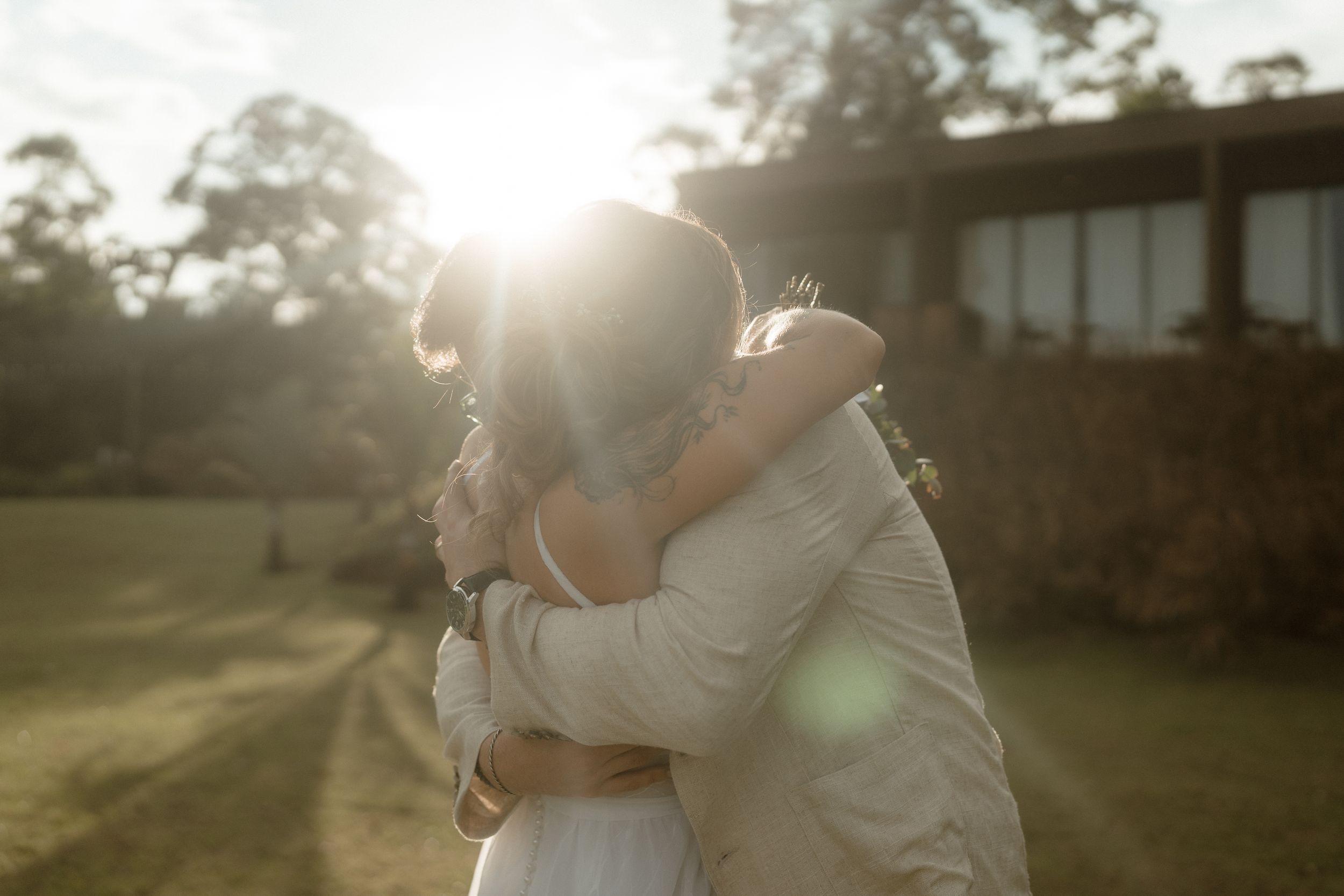 Romantic sunset embrace between couple in wedding attire with golden sunlight.