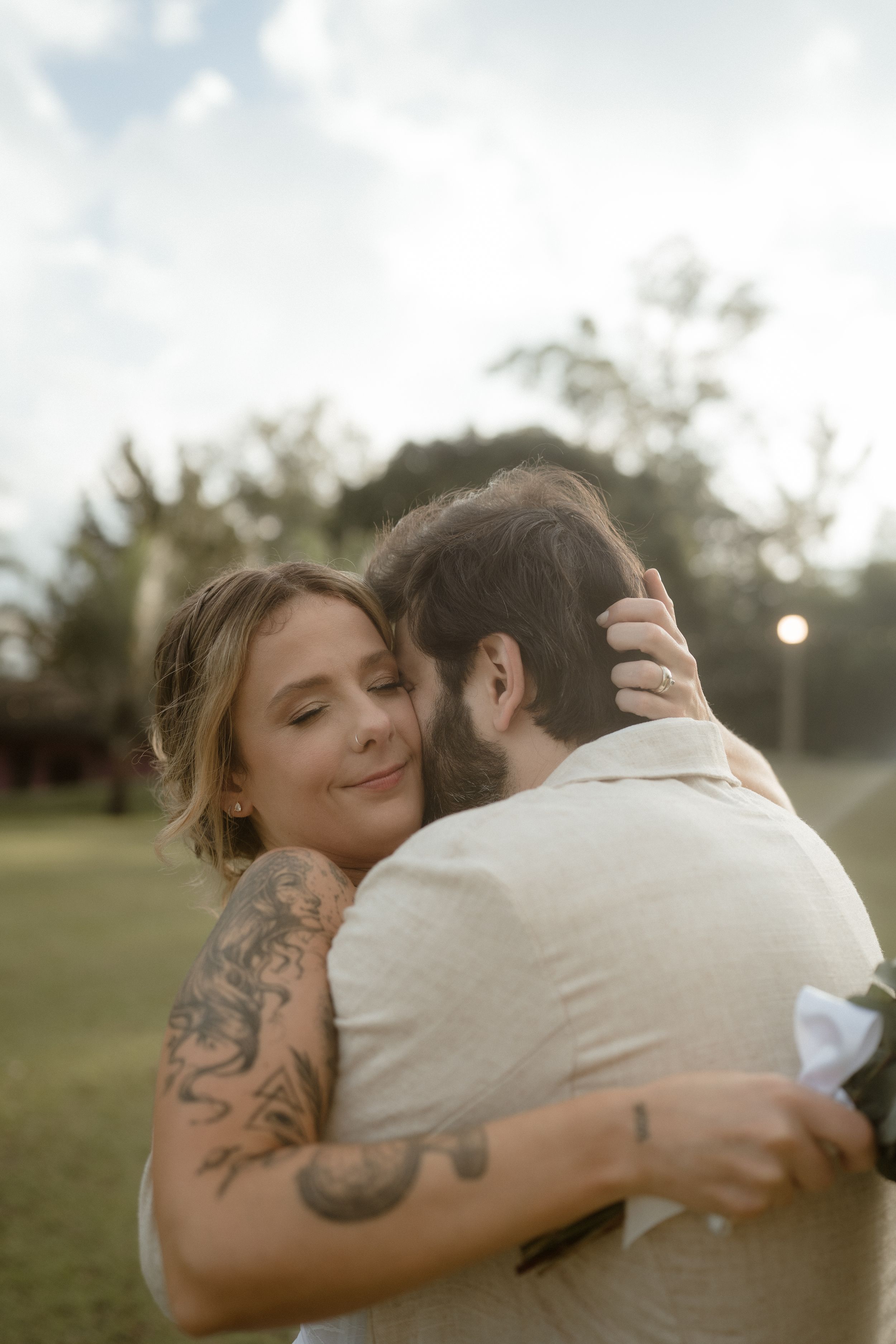 Intimate embrace between newlyweds showing visible tattoos in outdoor garden setting.