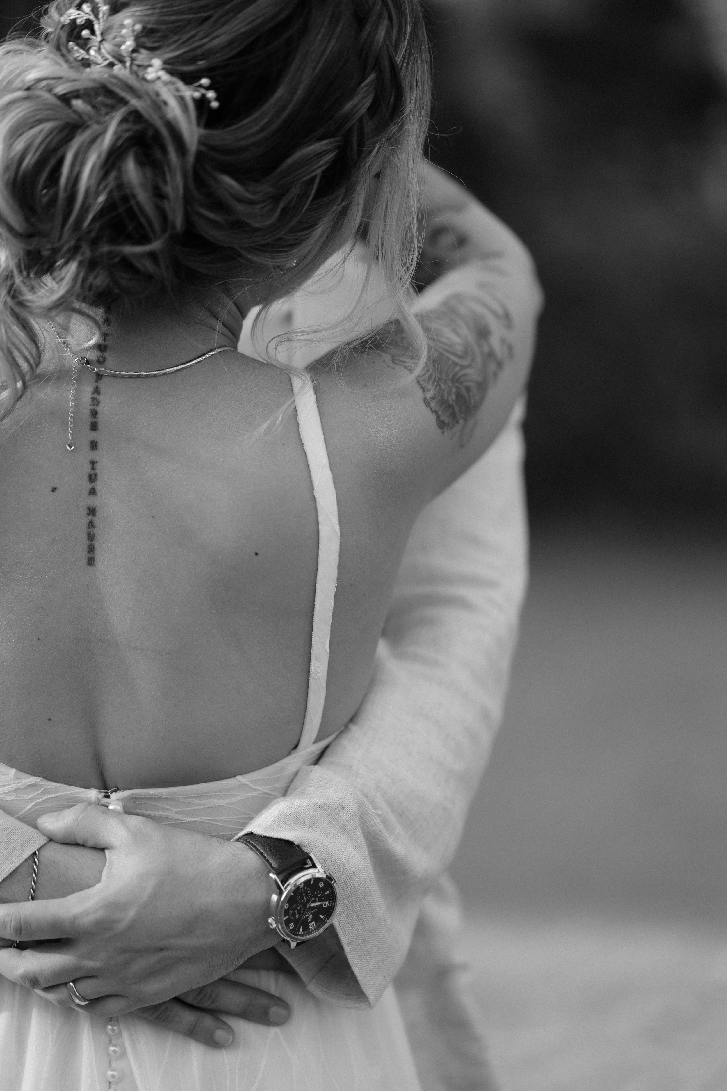 Black and white photo showing a delicate white dress strap and tattoo detail on a shoulder.