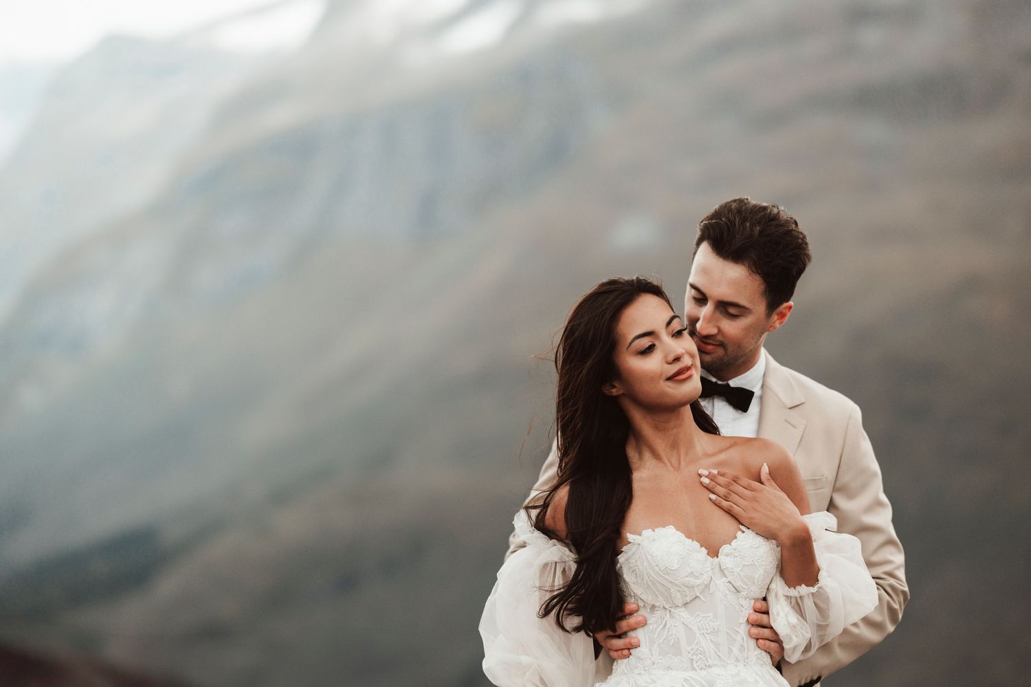 Newlywed couple embrace in an intimate moment against misty mountain backdrop during wedding photoshoot.