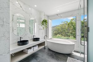 Luxurious modern bathroom with freestanding tub, black sinks, and marble walls featuring a large window with nature views.