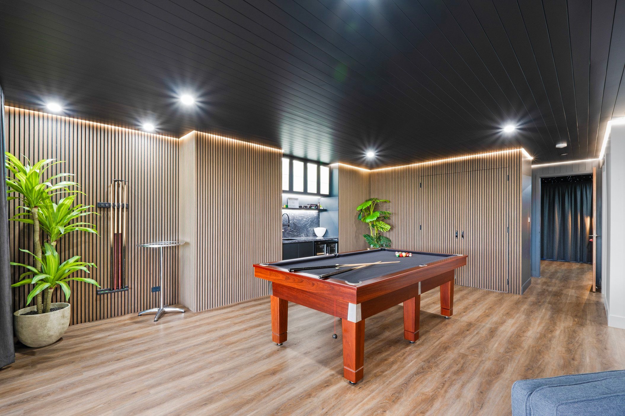 Modern game room with pool table, wooden walls and indoor plants.