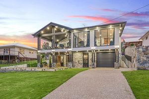 Modern two-story house with angled roof design illuminated at sunset featuring a manicured lawn and driveway.