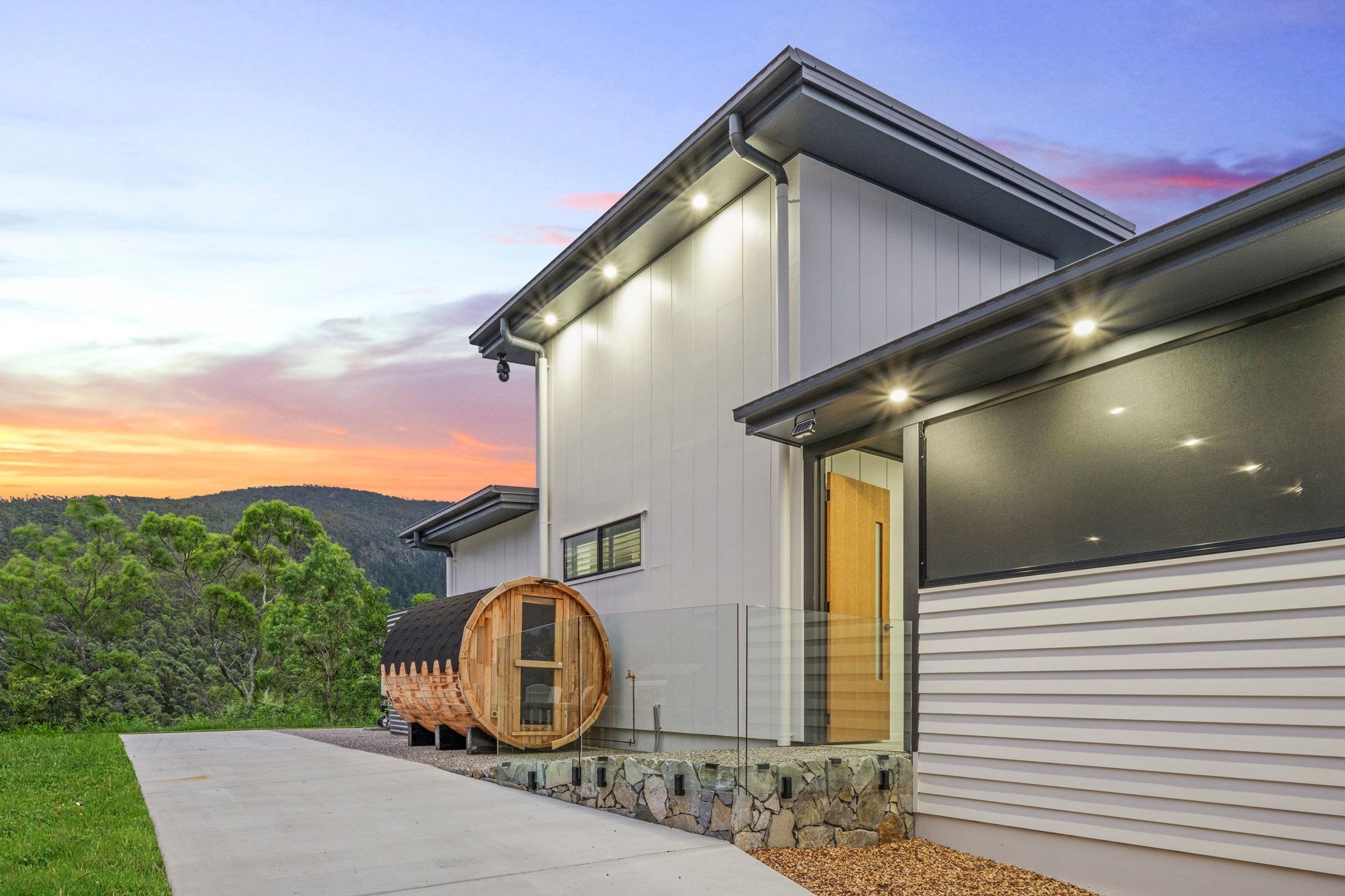 Contemporary house exterior with wooden barrel feature and scenic mountain backdrop at dusk.