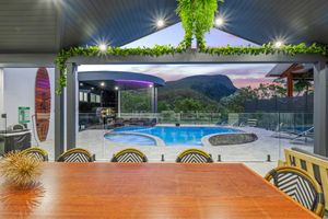 Covered outdoor dining area overlooking pool and mountain views with decorative lighting.
