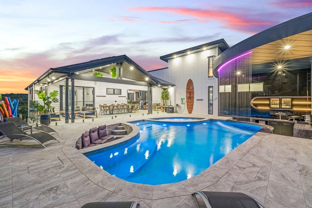 Stunning backyard with illuminated swimming pool and covered patio area at twilight.
