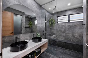Luxurious bathroom featuring dark marble tiles, twin vessel sinks and modern fixtures.