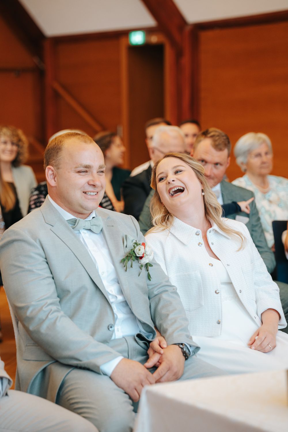 Wedding guests laugh together while seated during ceremony in a warm wooden reception hall.