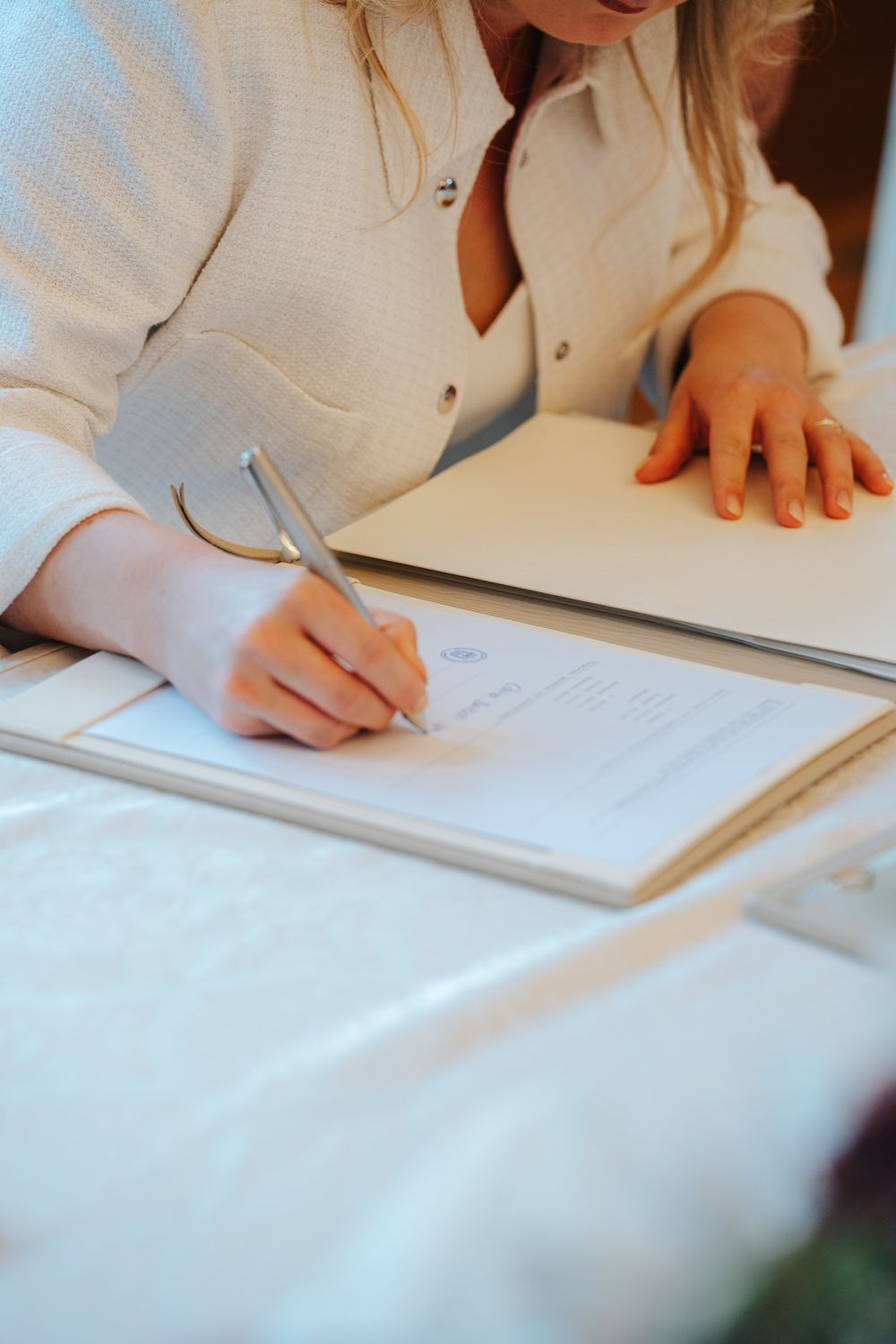 Close-up of hands signing a wedding document on a white tablecloth.
