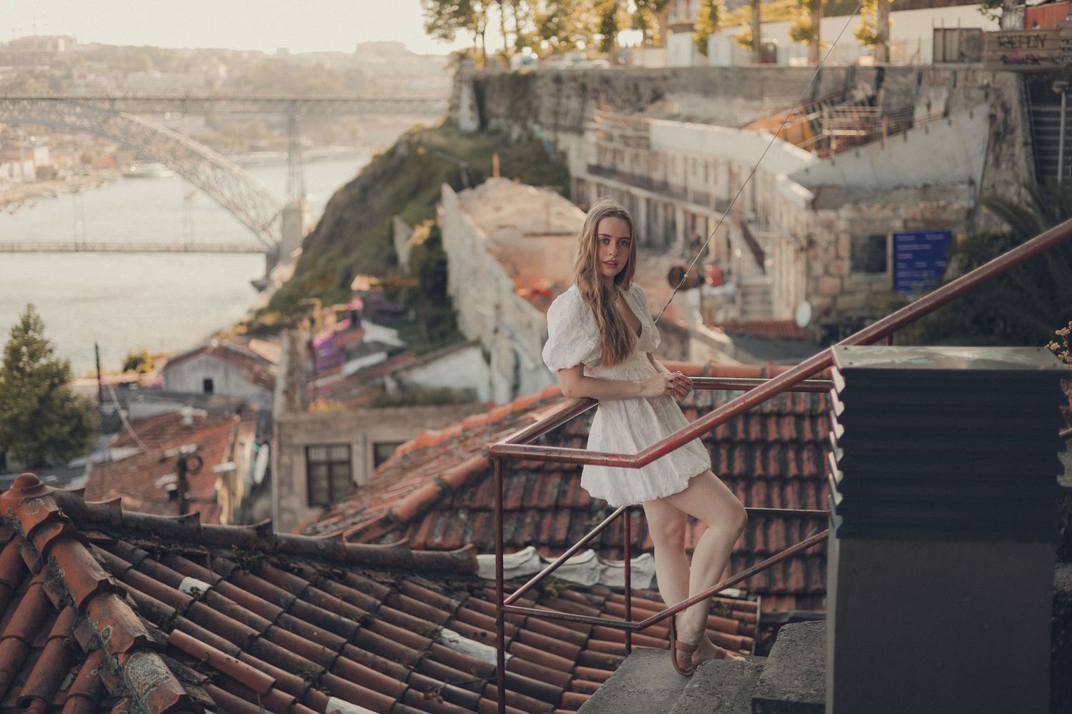 Woman in white dress twirling on rooftop terrace overlooking Porto's cityscape.