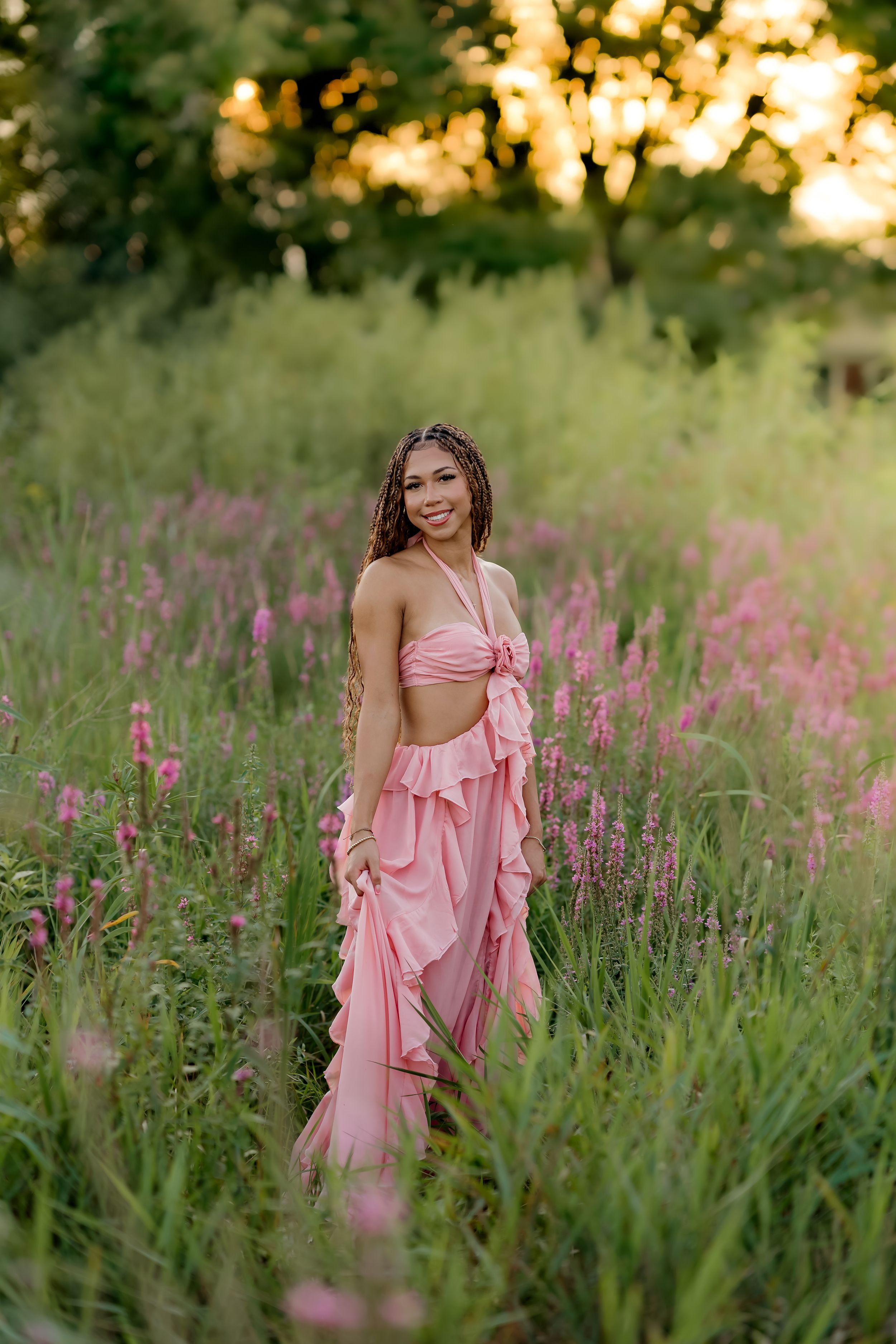 Young woman in pink two-piece ruffle outfit posing in a field of wildflowers at golden hour.