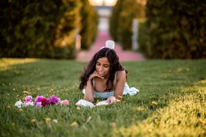 A person lies on grass reading a book beside pink flowers in a peaceful garden setting at golden hour.