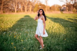 A white sundress flows in the golden light as someone poses in a wildflower meadow at sunset.