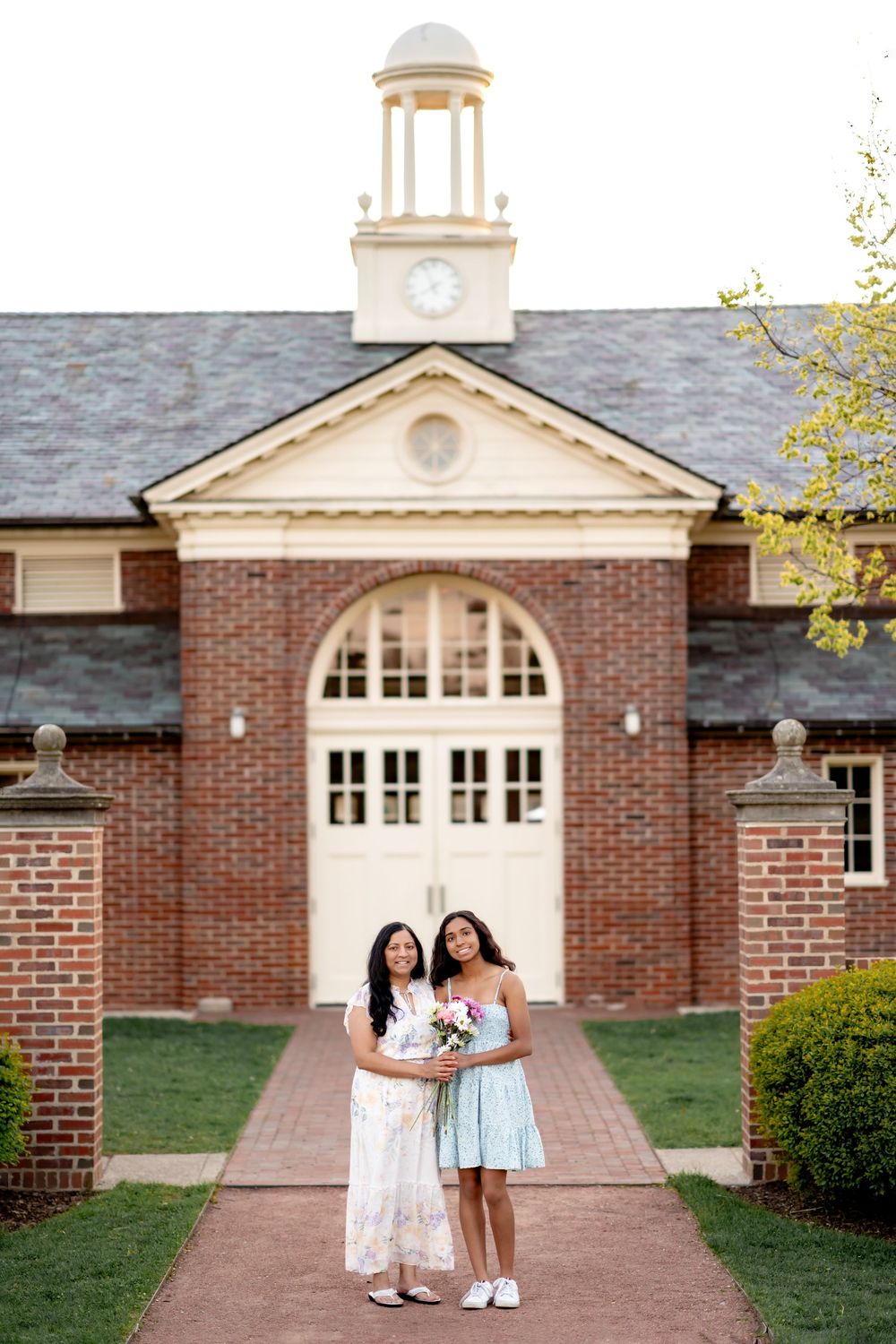 Two people stand together smiling on a brick pathway in front of a classic collegiate Georgian-style building with clock tower.
