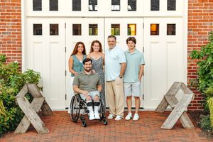 Five people pose together in front of a white wooden door with brick pillars and decorative crosses on either side.