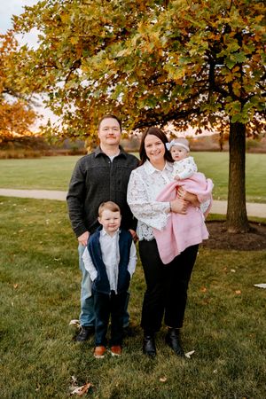 A group poses together on grass with fall foliage in the background during golden hour.