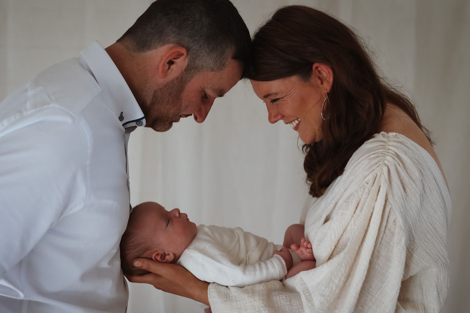 Intimate moment between mother and baby in white knit clothing by window.