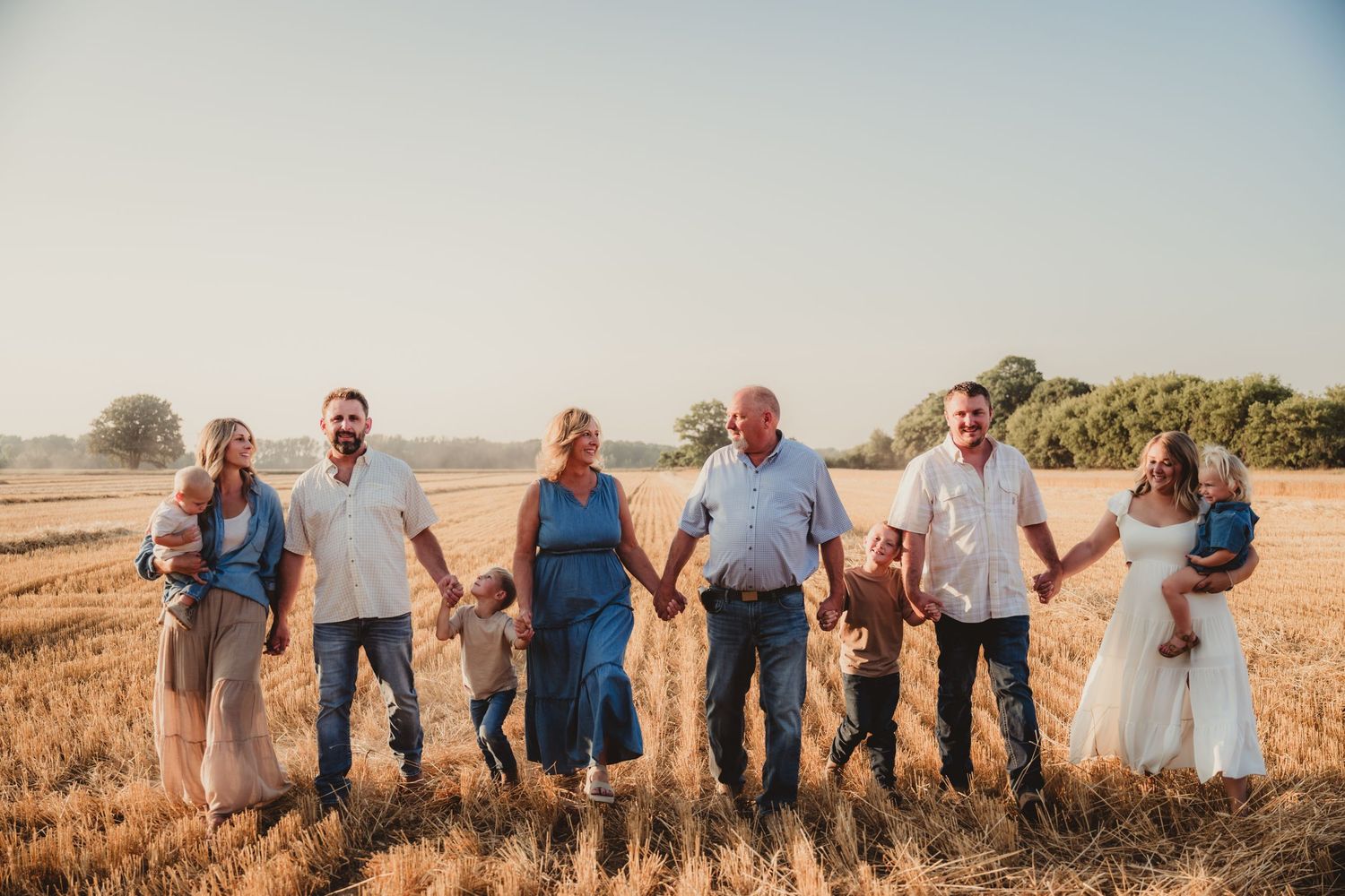 Group of people sitting on a sunny hillside overlooking a rural landscape during golden hour.