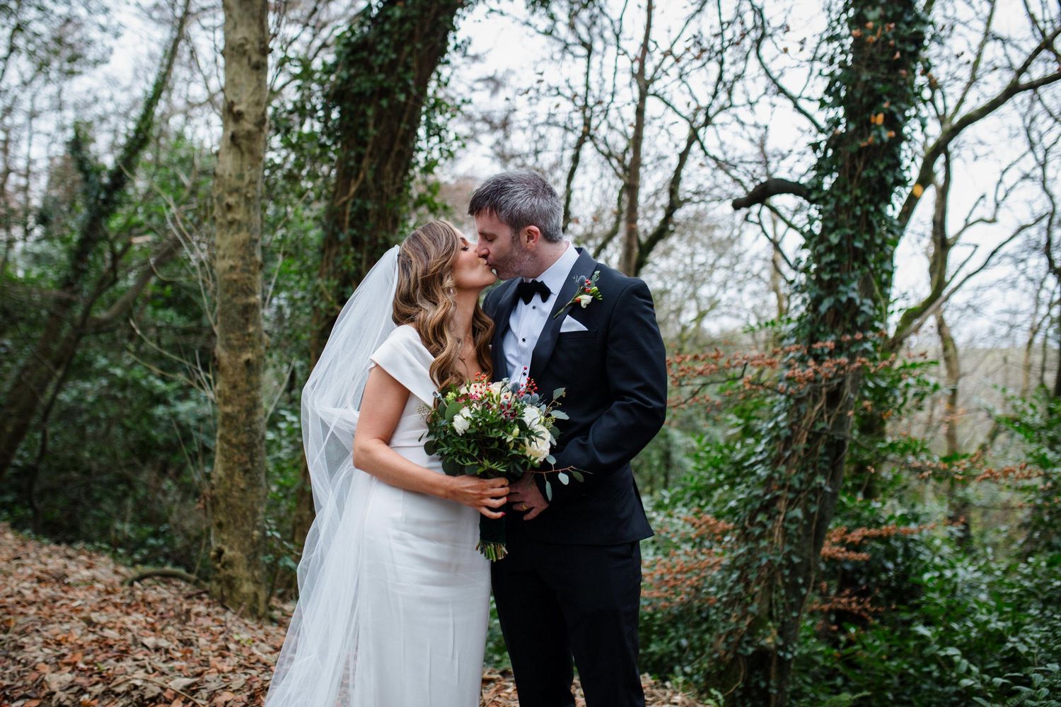 Newlyweds share an intimate moment in a wooded forest setting during their winter wedding ceremony.