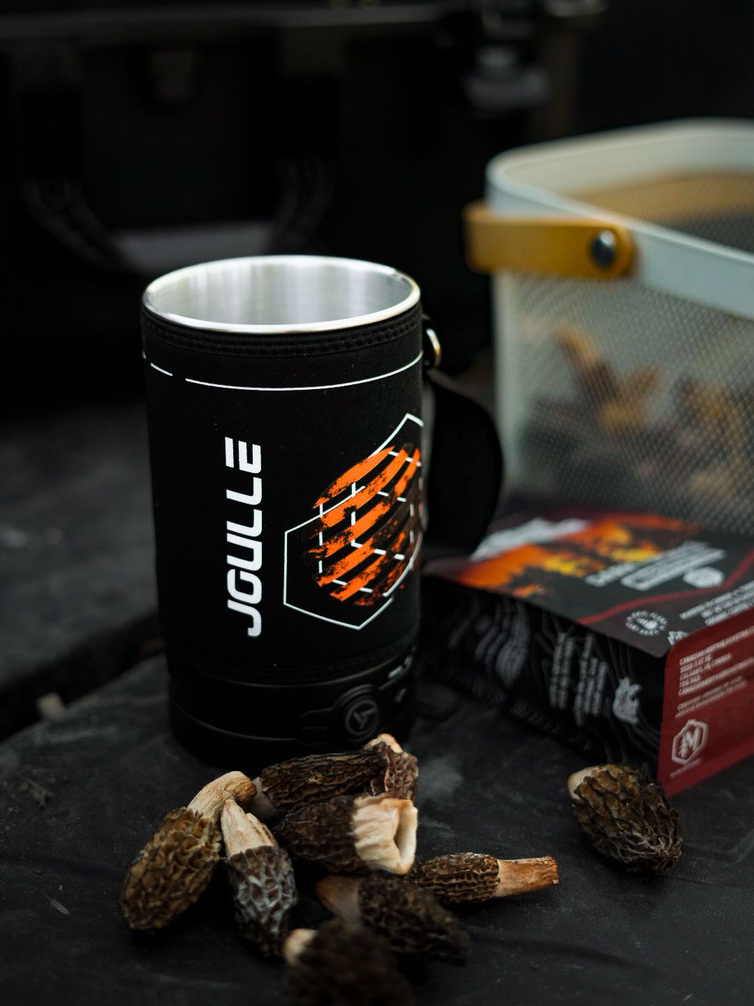 Coffee cups and brewing equipment arranged on dark surface with moody lighting.