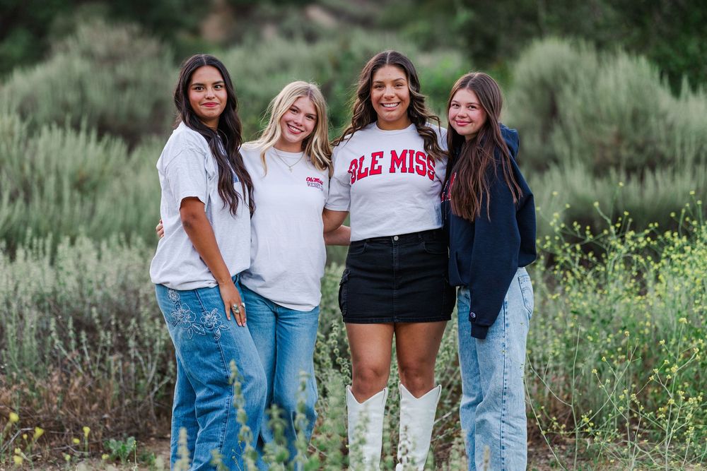 Four students in casual outfits stand together outdoors against green sage brush background.