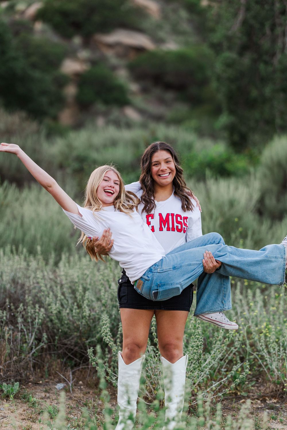 Two friends having fun outdoors, one wearing a white shirt and another in Ole Miss apparel among green vegetation.