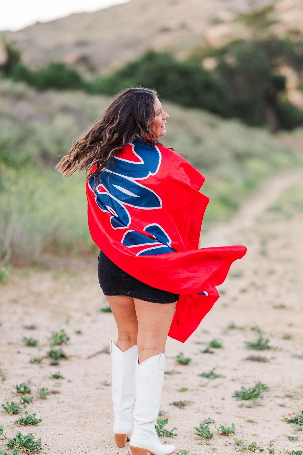 Person wearing white boots stands on a desert trail with a red flag flowing in the wind. Graduation photos