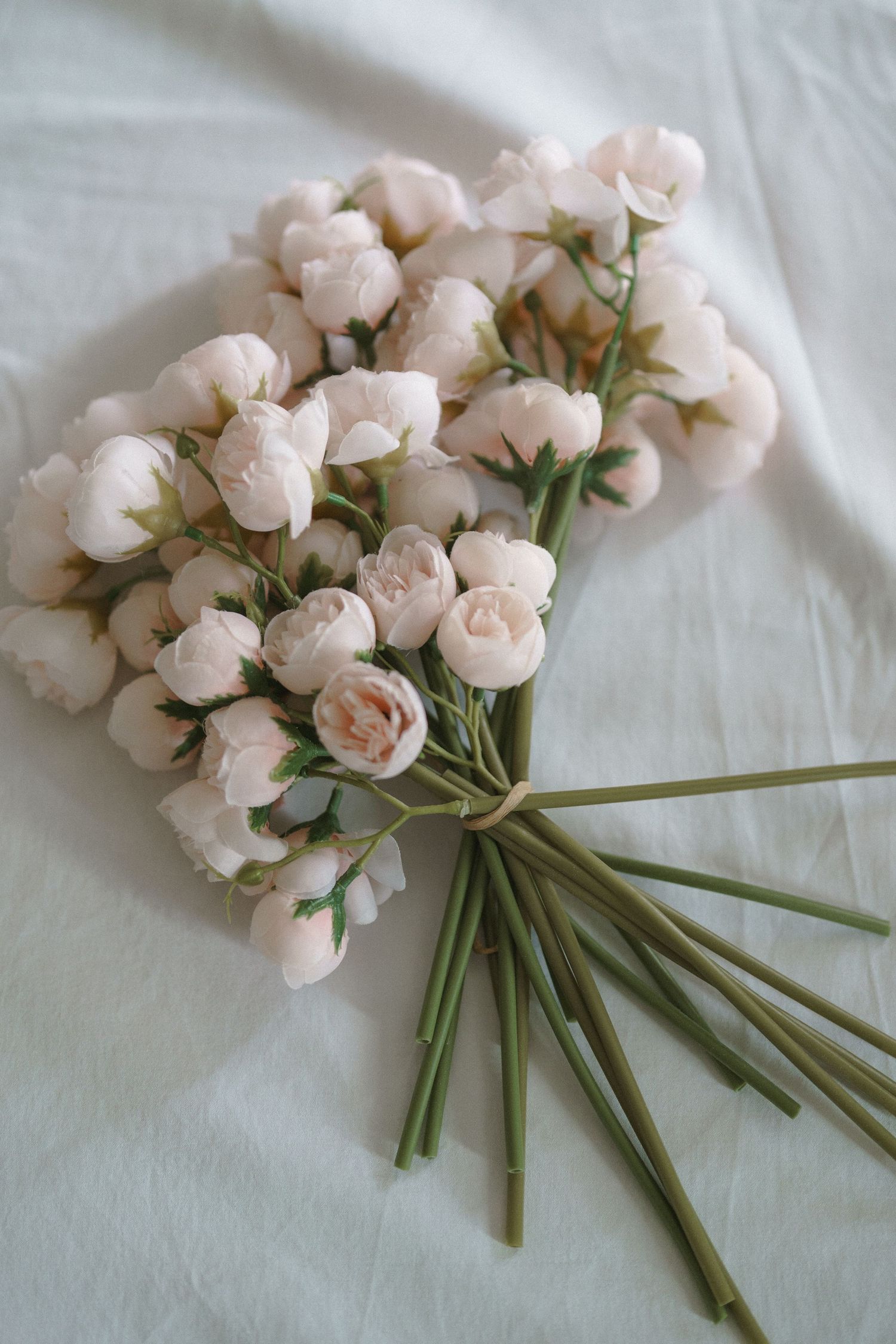 A delicate bouquet of light pink spray roses with green stems arranged on a white textured background.