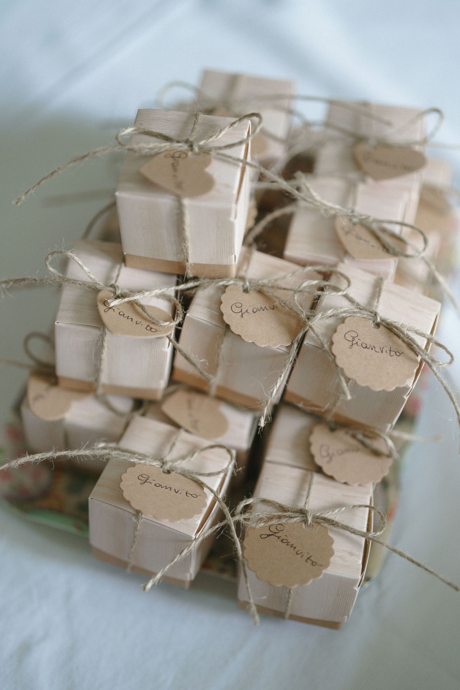 Small white favor boxes with kraft paper tags and twine bows arranged neatly on a light surface.