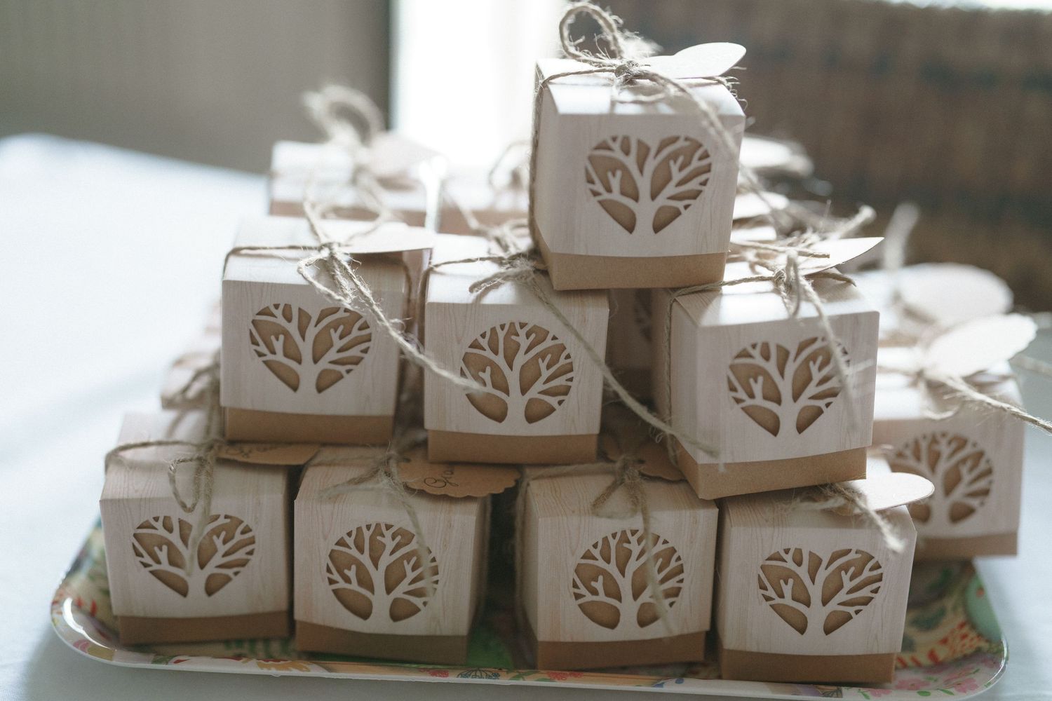 Small white favor boxes with tree designs stacked in a pyramid display at a wedding or special event.
