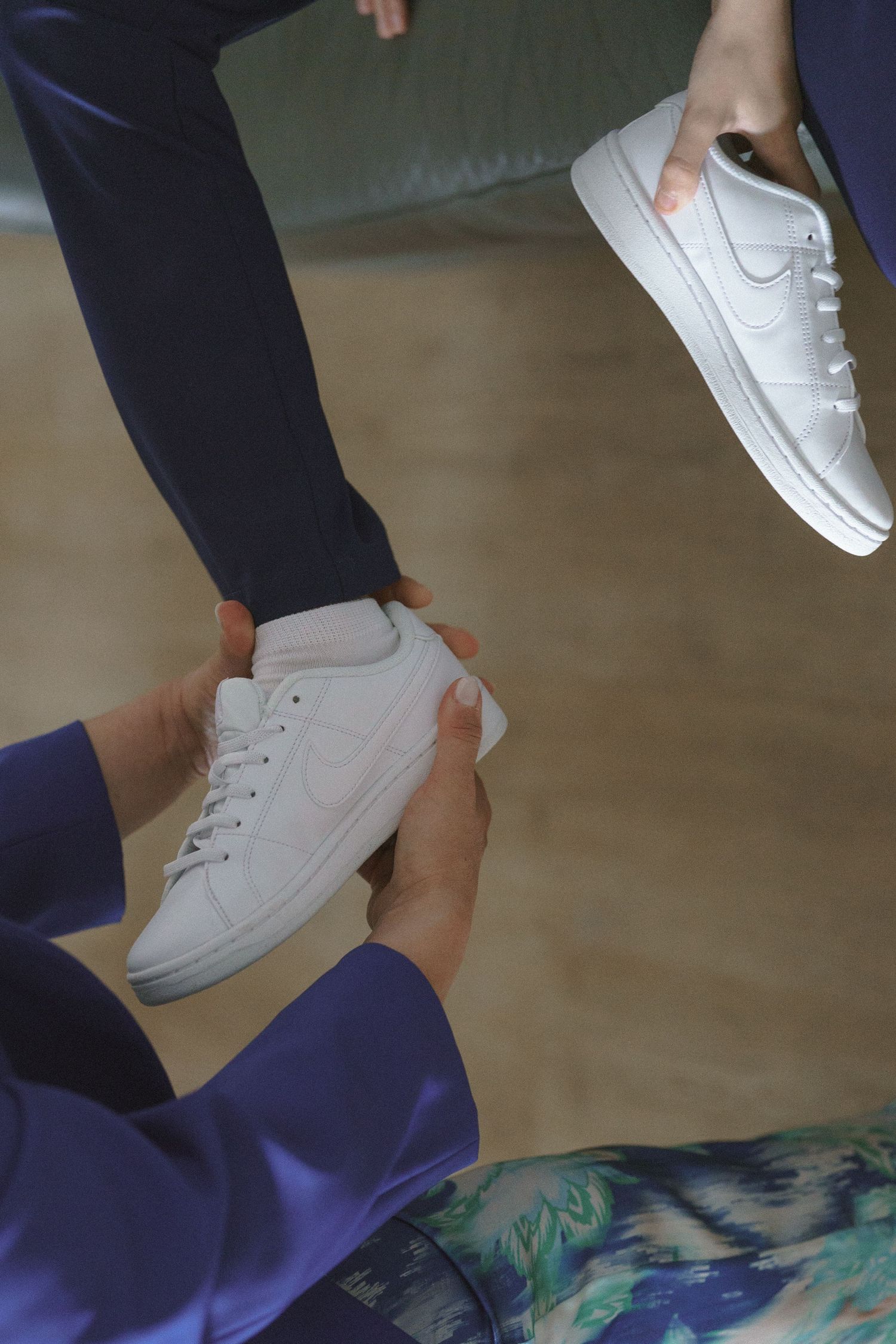 Hands adjusting white sneakers on feet with navy pants, showing shoe fitting or styling process.