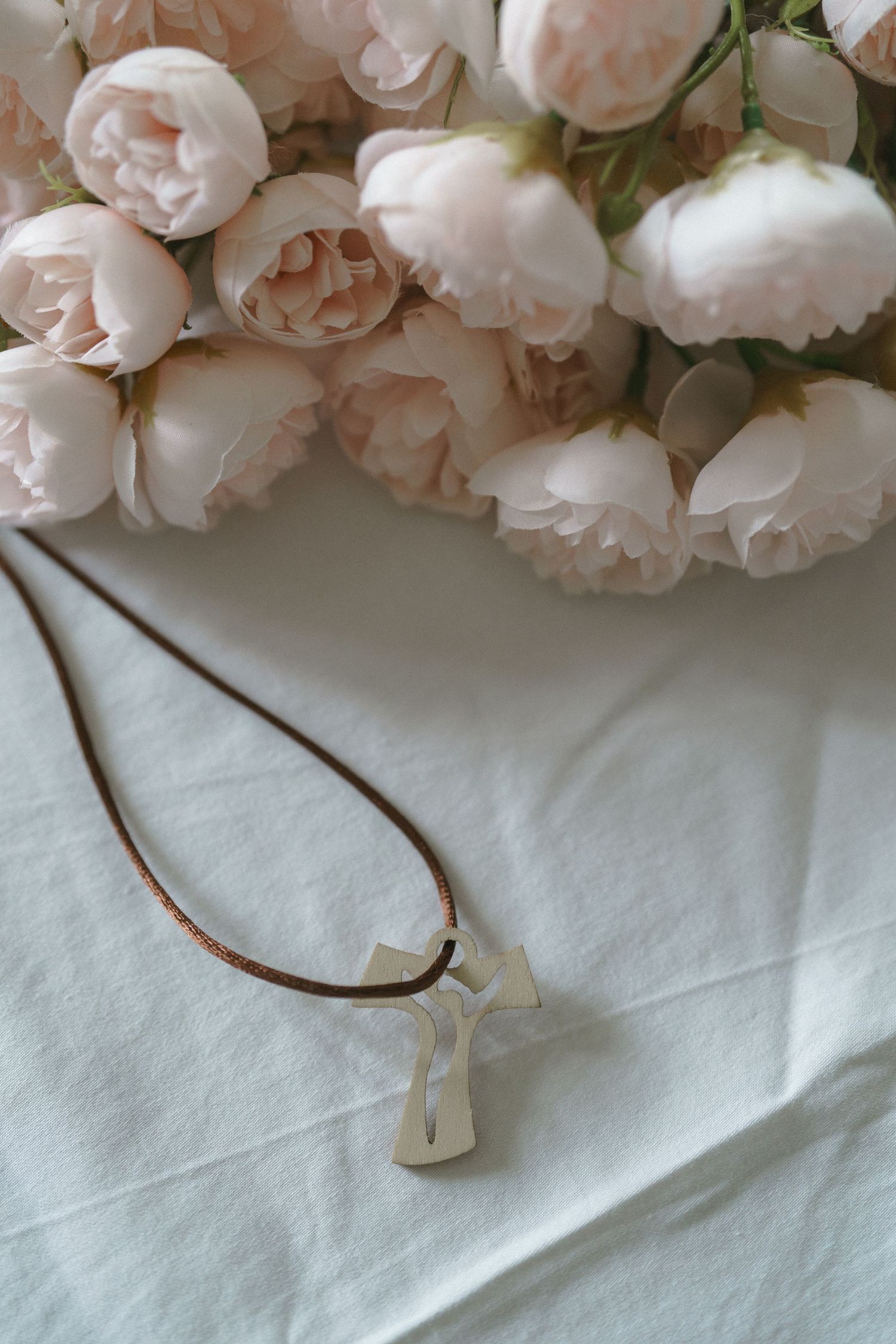 A delicate pendant necklace on a white surface with soft pink and white garden roses in the background.