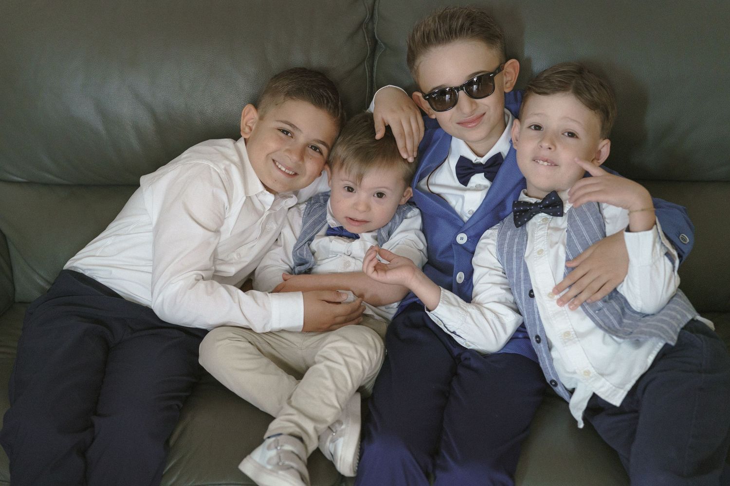 Four boys dressed in formal attire pose together on a dark leather couch.