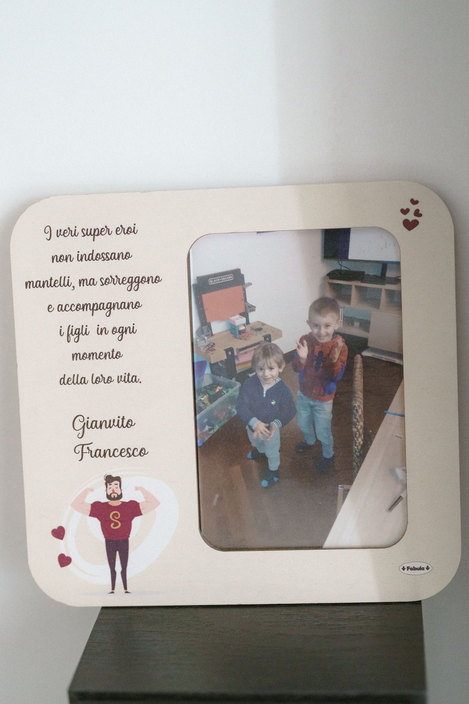 A decorative white photo frame with Italian text and a cartoon character illustration sits on a dark surface.
