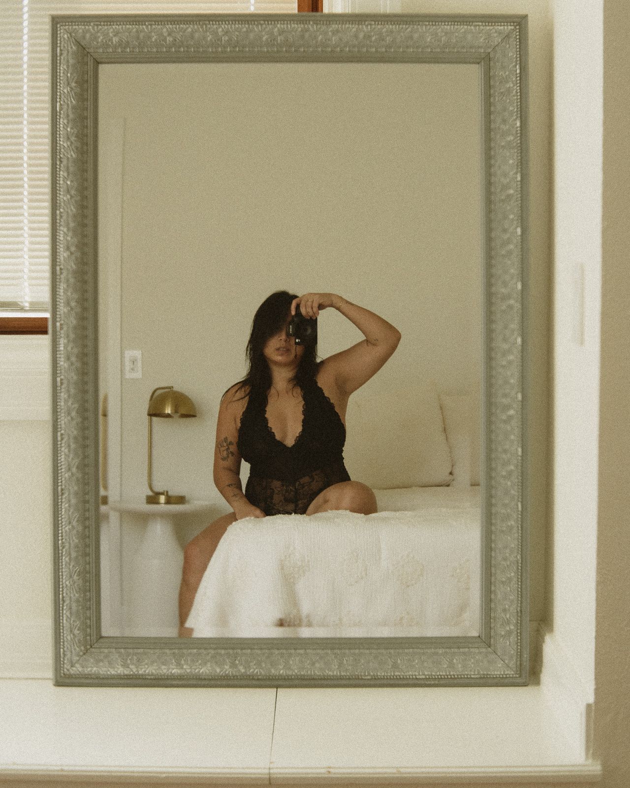 Mirror reflection showing a person taking a self portrait in a gray ornate frame mounted on a white wall.
