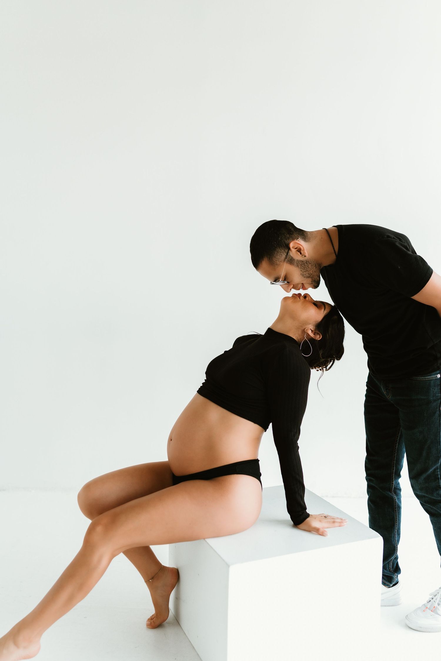 Artistic maternity photoshoot featuring intimate poses against a white backdrop.