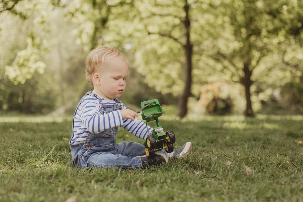 boy sits on grass playing with tractor