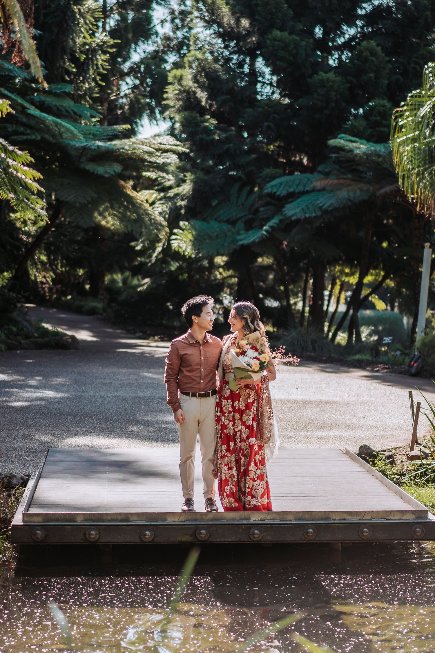 A couple walks together on a path surrounded by lush ferns and greenery in a romantic garden setting.