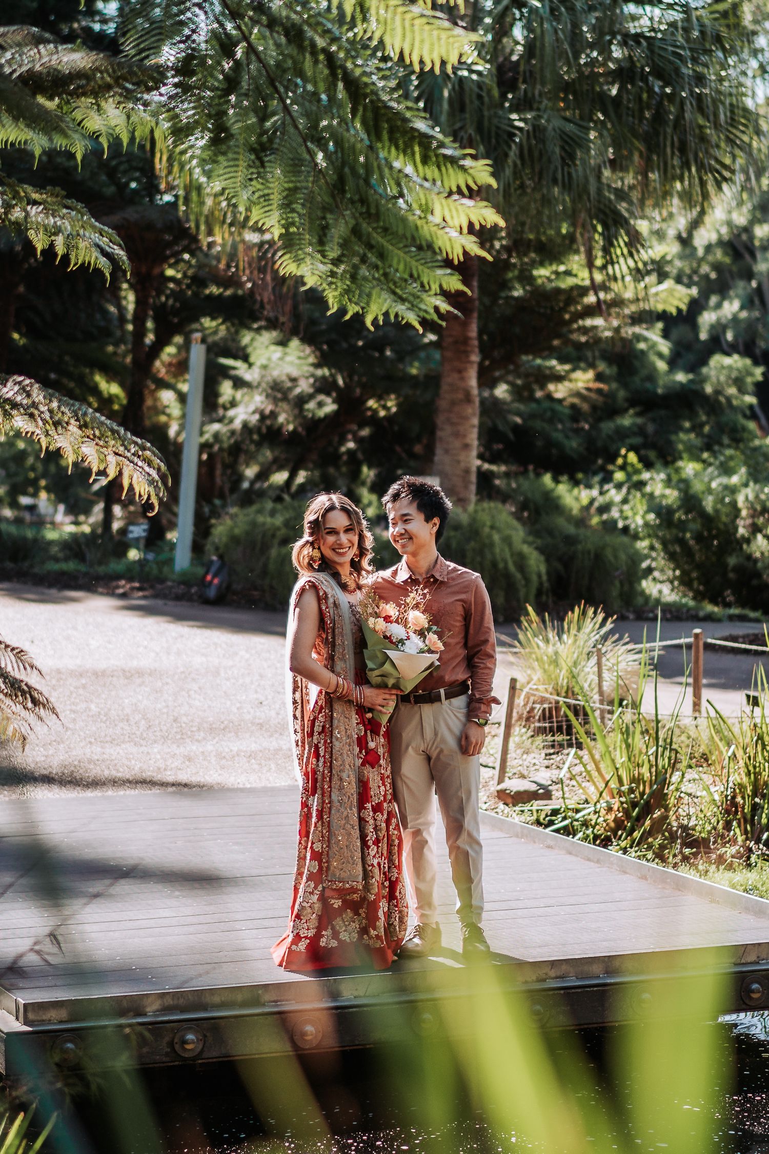 A couple shares a romantic moment on a garden pathway surrounded by tropical palm trees and lush greenery.