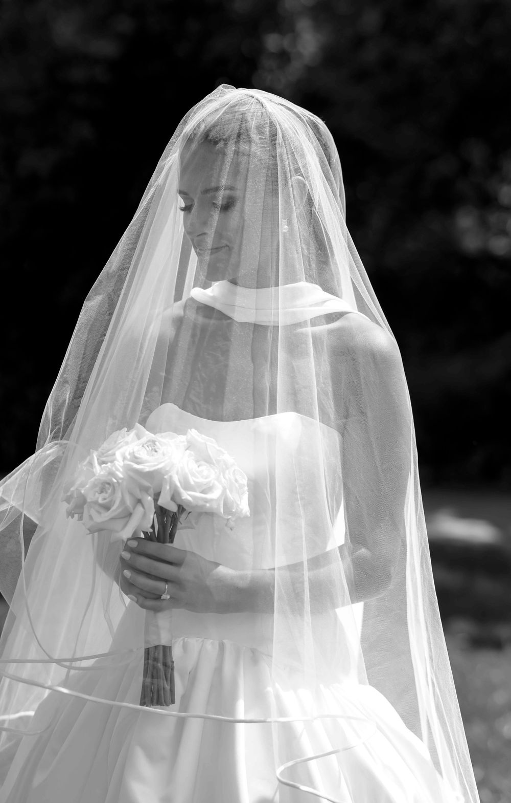 A black and white photograph shows a bride in a flowing white veil from behind, creating an ethereal silhouette effect.