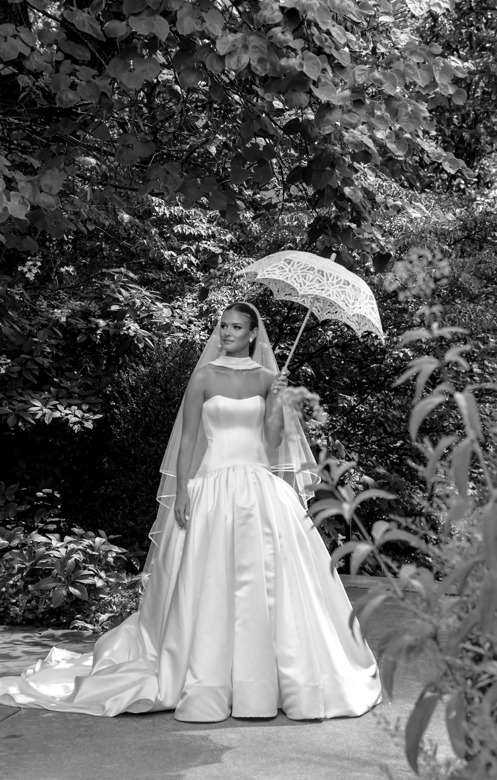 A sequence of black and white photos showing a white wedding dress with a flowing train in an outdoor garden setting.