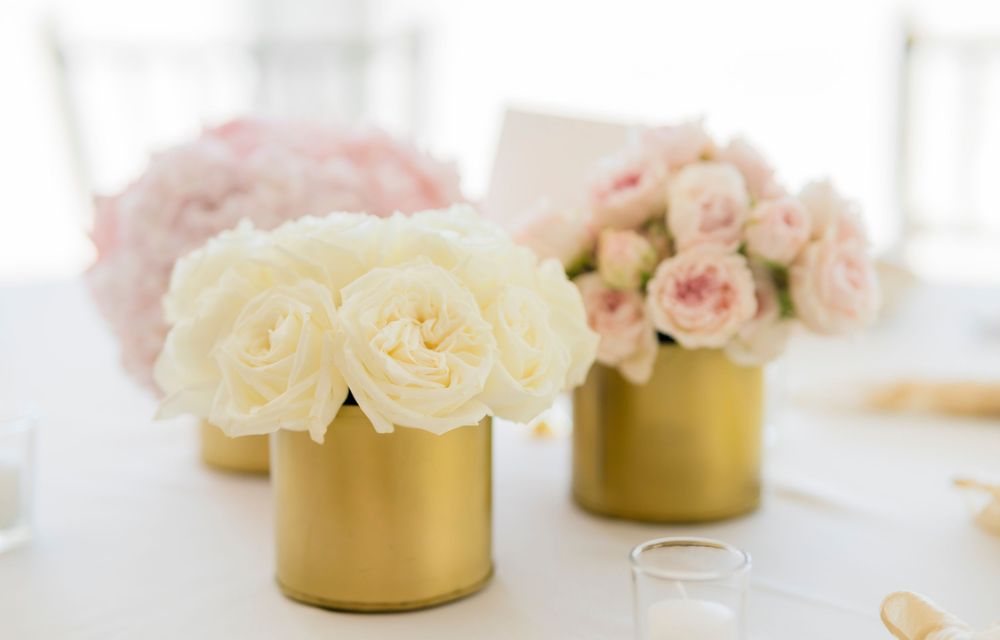 Fresh white and pink roses arranged in elegant gold metallic vases on a white table surface.