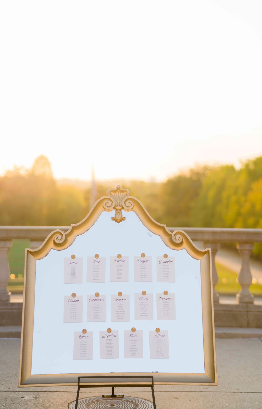 A decorative gold-framed seating chart display on a stand captured during golden hour sunset outdoors.