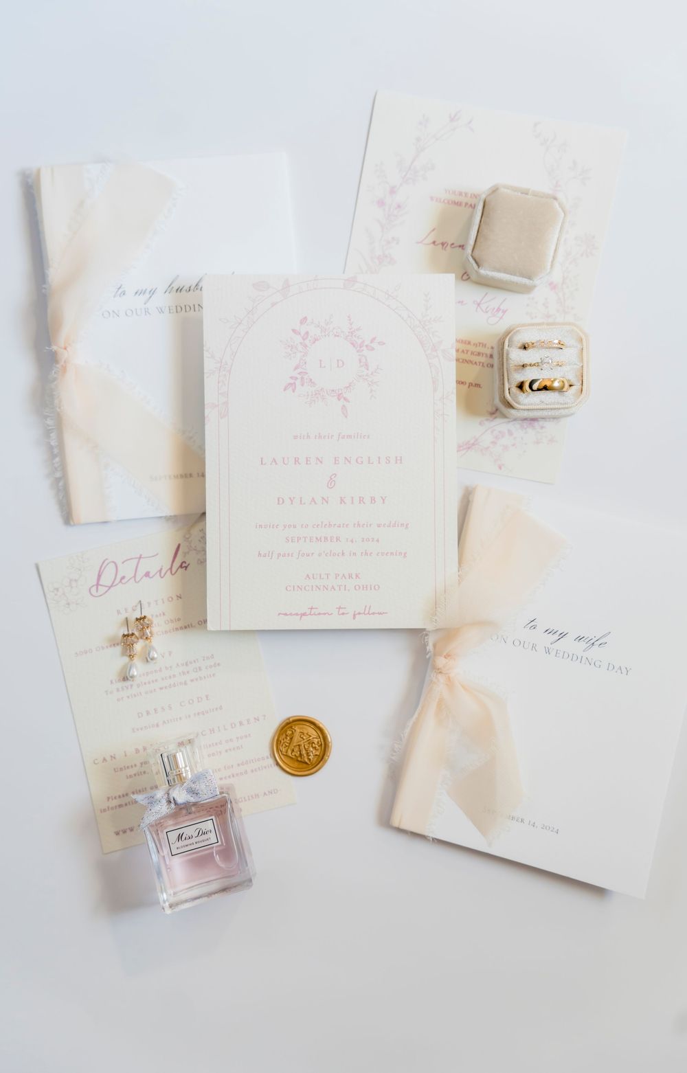 Elegant wedding invitation suite with perfume bottle, wax seal and ribbon in soft neutral tones on white background.