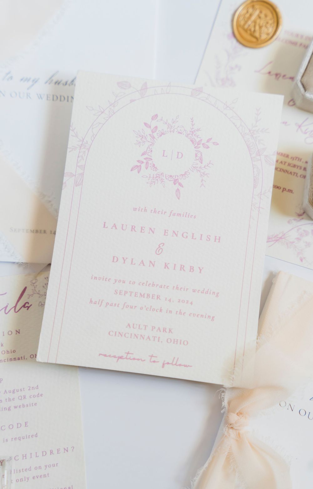 Elegant wedding invitation with soft pink floral design and gold wax seal on white paper.