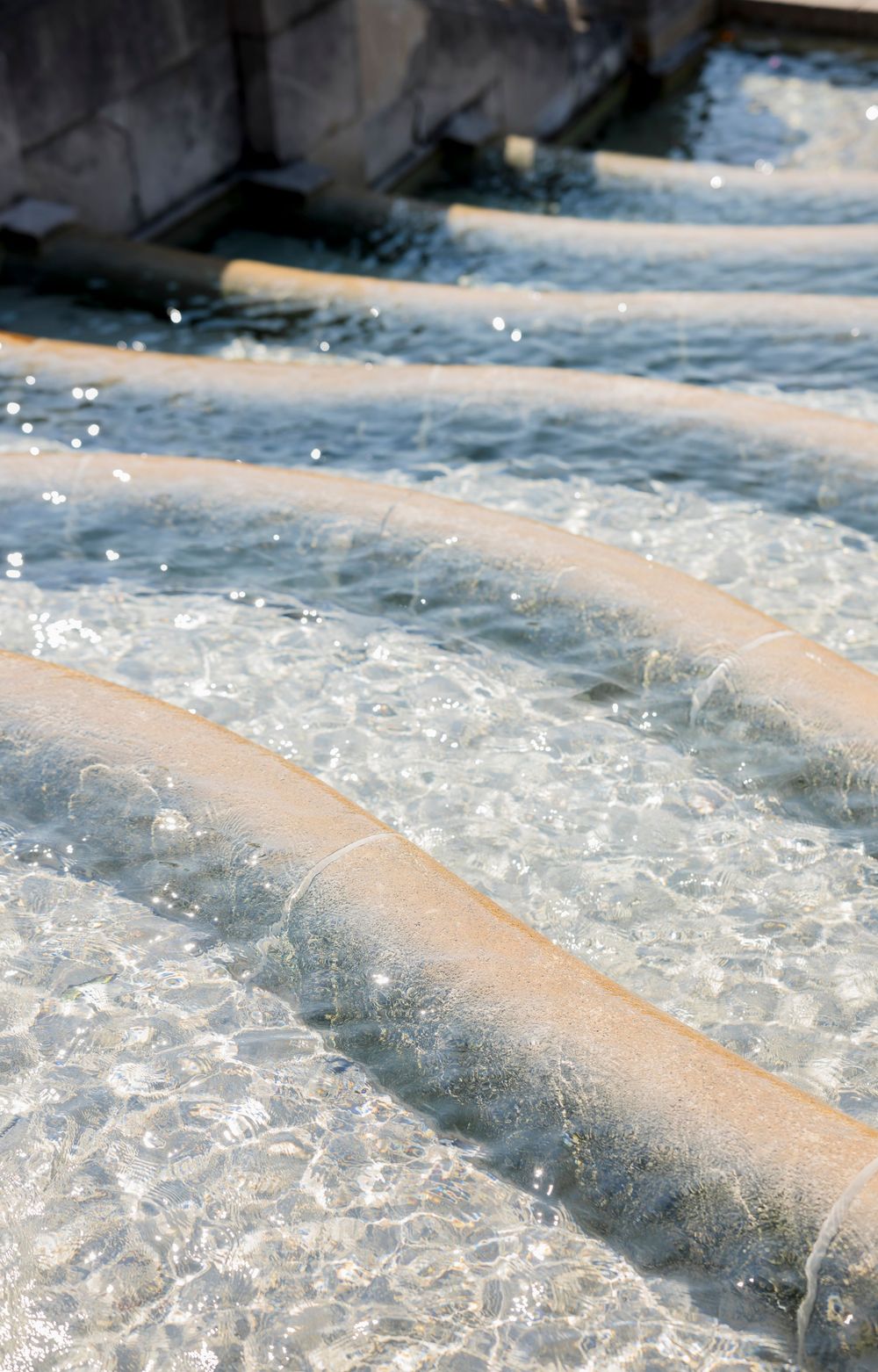 Cascading water flowing over concrete steps creating a serene waterfall pattern in sunlight.